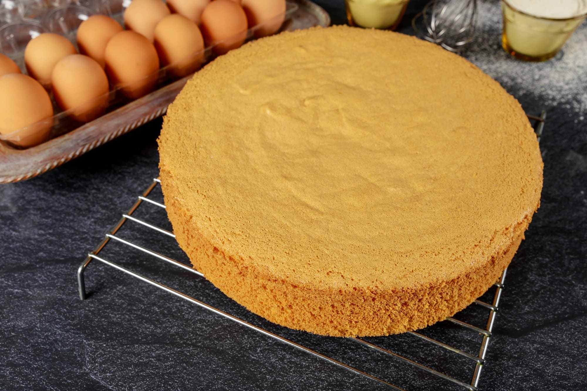 Homemade sponge cake on black background with eggs, flour and whisk. Bakery concept.