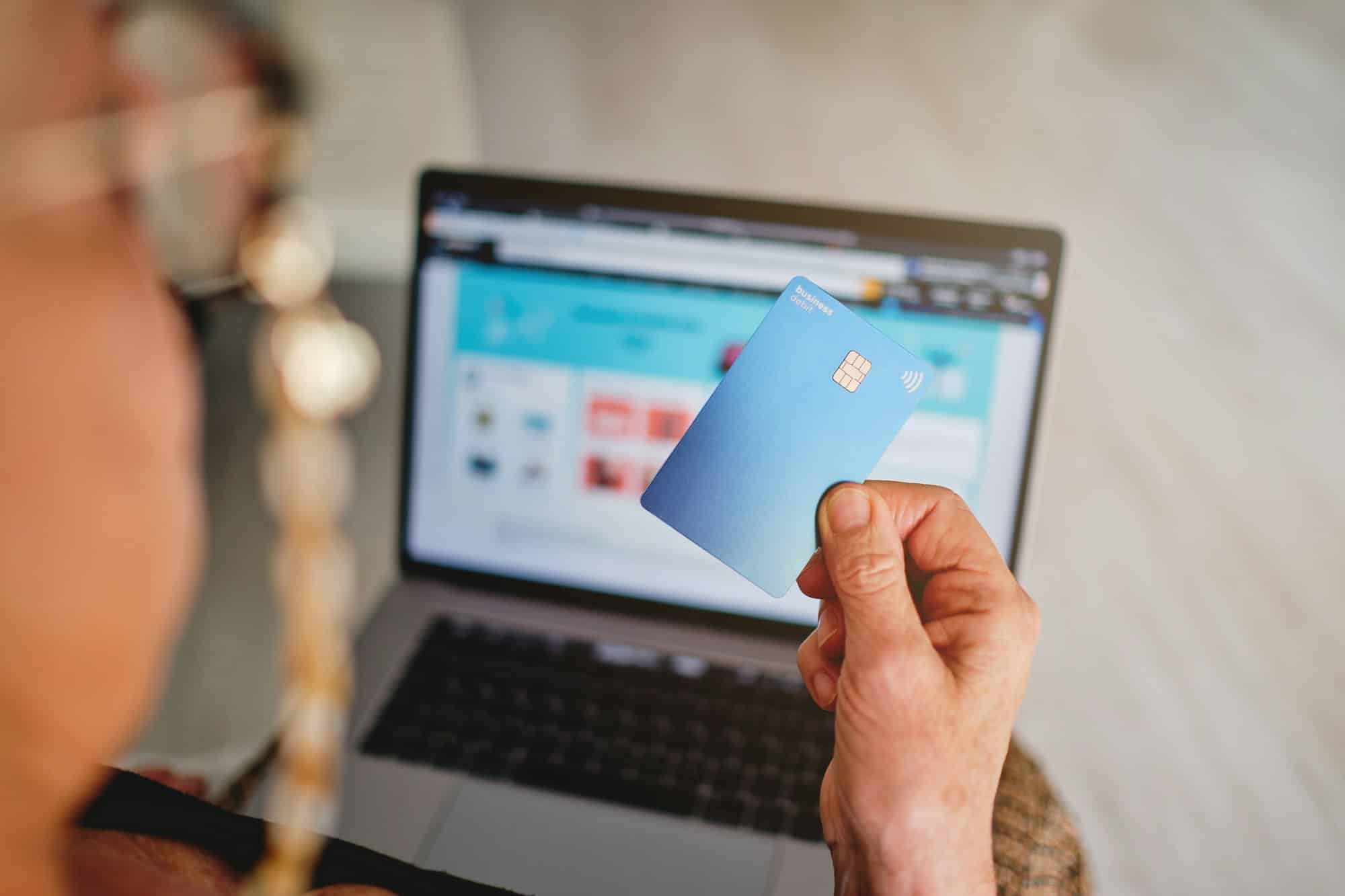 Adult woman holding a card with her hand in front of the computer about to pay for a purchase